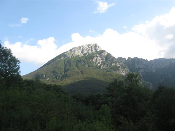 Rocky peak rising above green forest, white clouds in blue sky