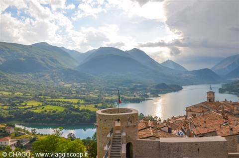 Stone tower with flag above Barrea rooftops and lake surrounded by mountains