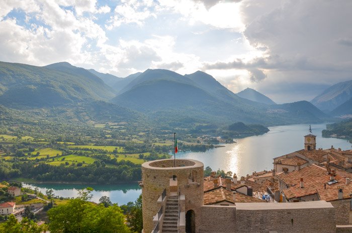 Torre in pietra con bandiera sopra i tetti di Barrea e il lago circondato dai monti
