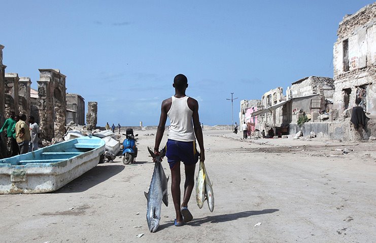 Pescatore con pesci appena pescati cammina tra edifici in rovina e barche