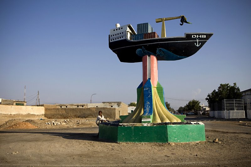 Monumento a forma di nave cargo su colonna dipinta, un uomo seduto vicino