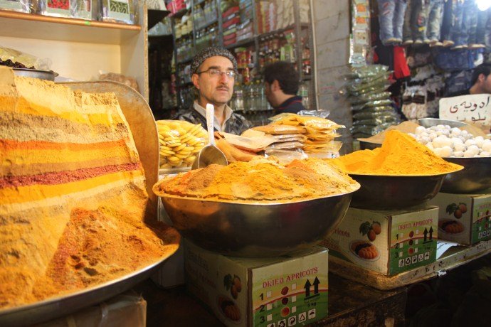 Venditore in mercatore di spezie, vasche metalliche piene di curcuma e peperoncino