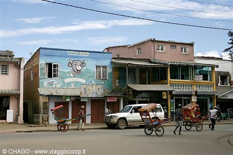 Men pull rickshaws past colorful buildings and a pub along the street