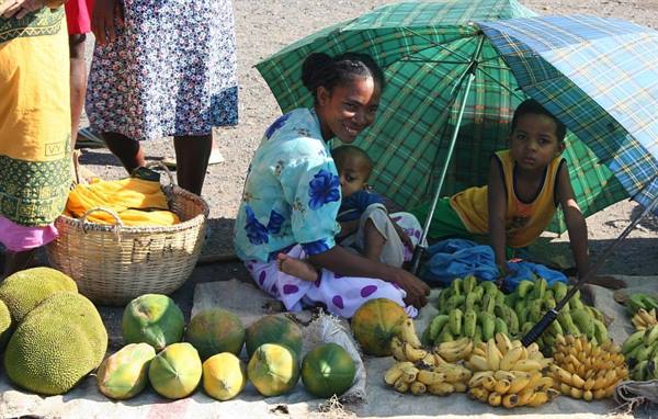 Woman and children selling bananas, papayas and jackfruit under a green umbrella at market