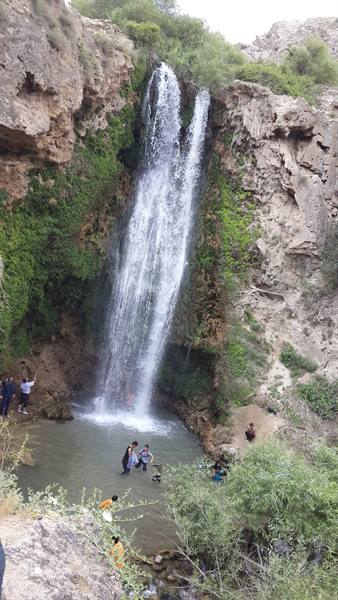 Waterfall over mossy rocks, tourists wading at the base