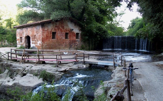 Vecchio mulino in pietra rossa accanto a una piccola cascata e passaggio in legno