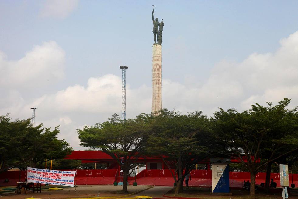 Colonna con statua dimani sopra alberi e tribune rosse, Benin