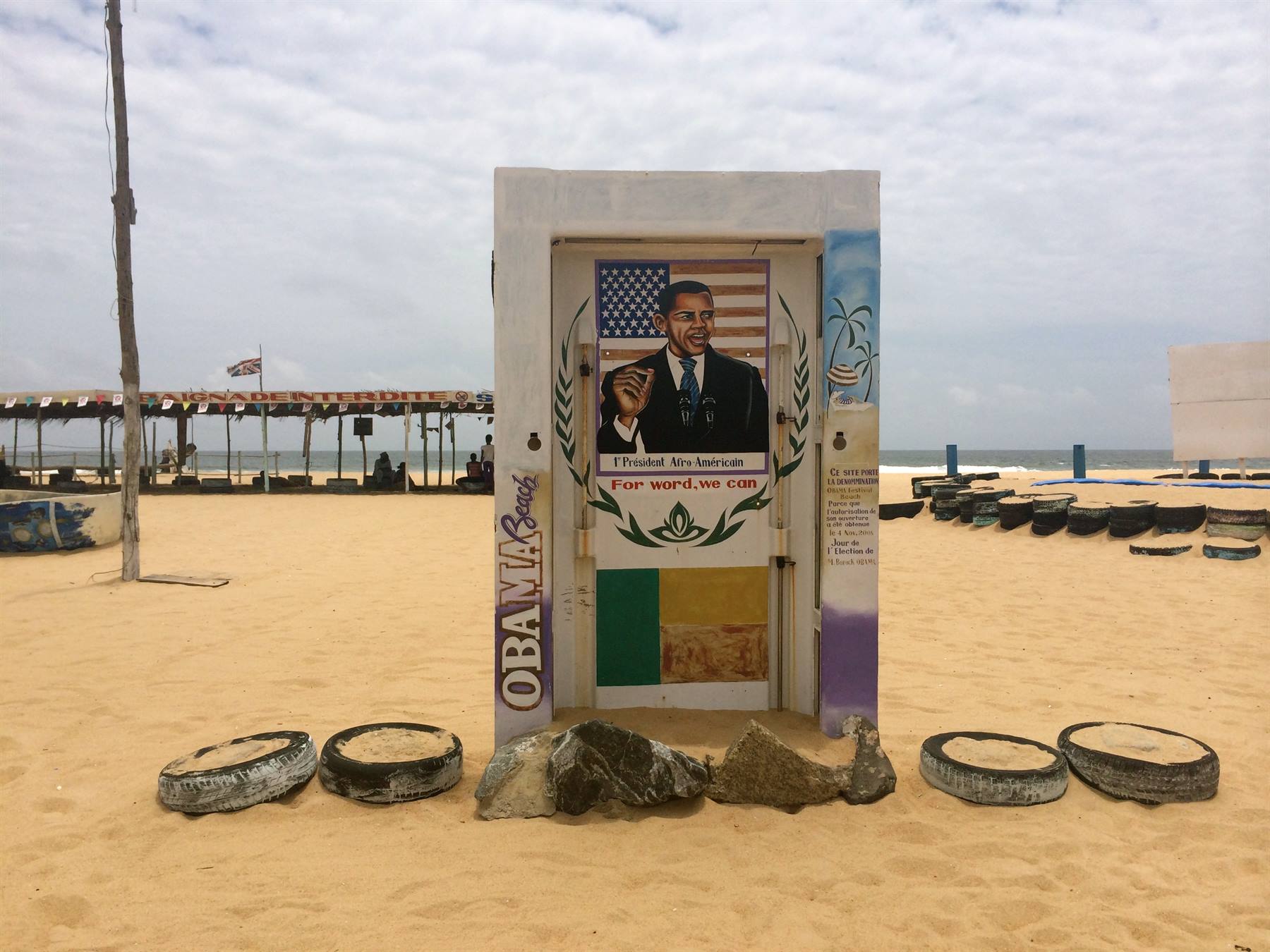 Porta dipinta con ritratto di Obama su spiaggia sabbiosa, gomme e pali intorno