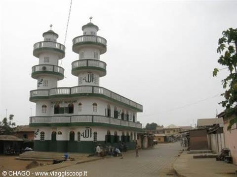 White and green mosque with two terraced minarets, dirt street with passersby