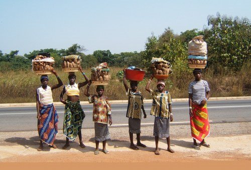 Donne africane con ceste di frutta in equilibrio sulla testa lungo l'asfalto