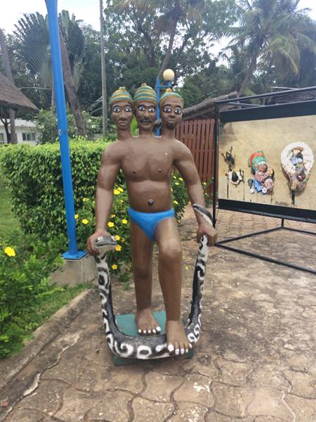 Three-headed statue in slippers standing on painted snake, tropical garden