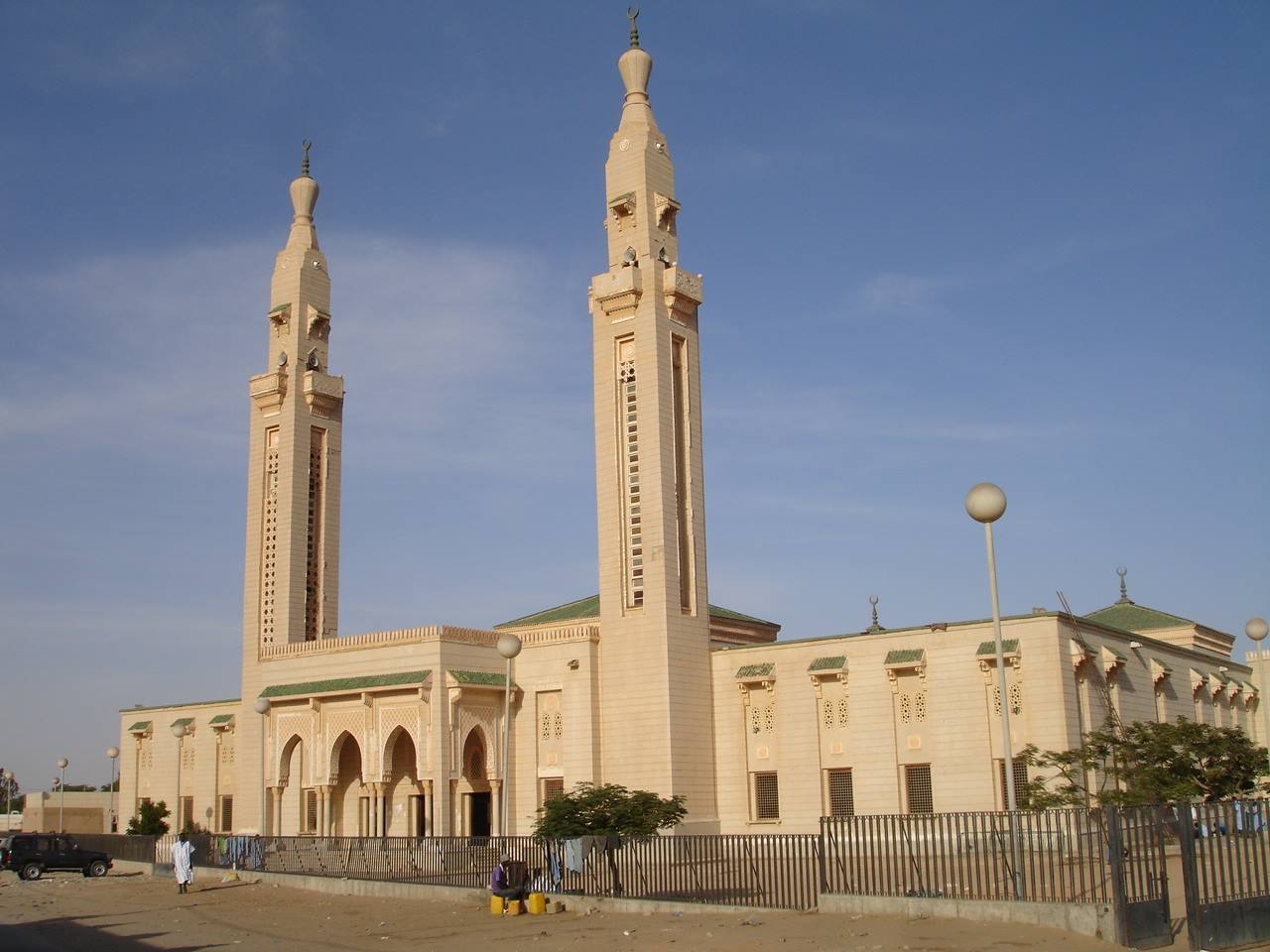 Moschea in pietra chiara con due alti minareti, cielo azzurro, mercato ai piedi