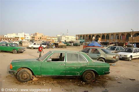 Old green car abandoned on the sand, market of a Saharan town