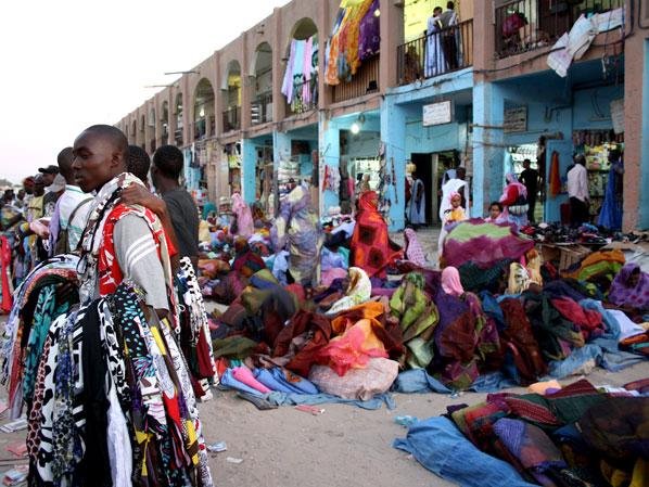 Mercato di stoffe colorate sotto gli archi, venditori e compratori tra teli sparsi