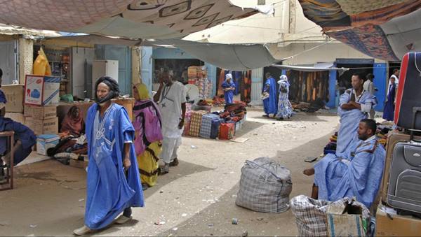 Covered market with colorful fabric awnings, men in blue boubous, suitcases for sale