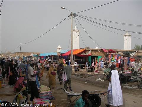Street market with colorful stalls, people walking and white minarets in the background