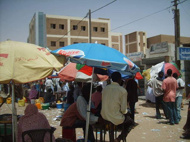 Mercato di strada con ombrelloni colorati e insegne in arabo tra gli edifici