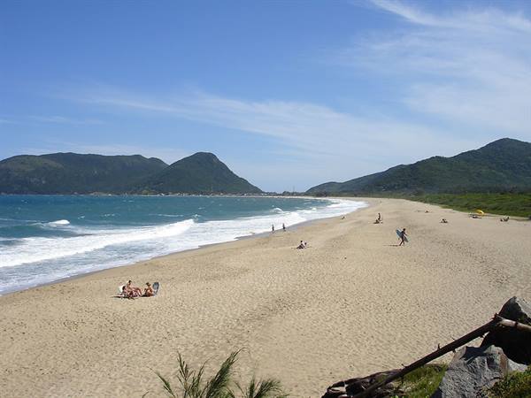 Sandy beach with swimmers, waves and green mountains under blue sky