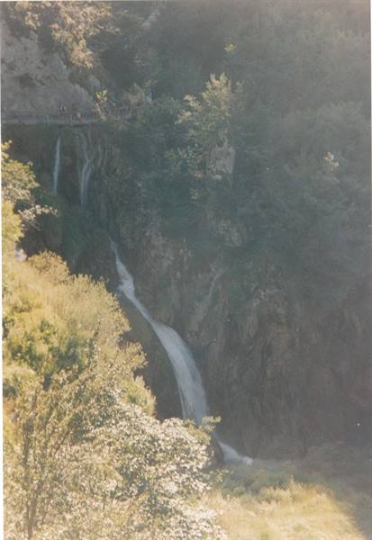Waterfall flowing down forested rocks, walkway with tourists above