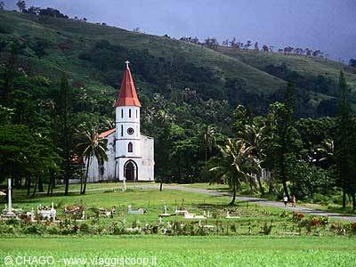 White church with red steeple among palms, green churchyard and hills