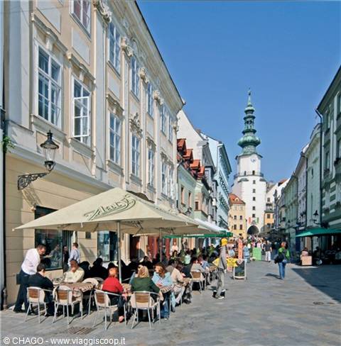 Sidewalk café with umbrellas on a pedestrian street, St Michael's tower behind
