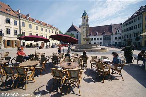 Café tables with red umbrellas on Bratislava square, fountain and church