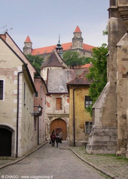 Cobbled alley with old houses, people walking, Bratislava Castle in the background