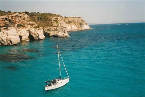 White sailboat anchored in turquoise cove with limestone cliffs
