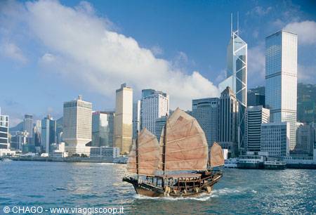 Brown-sailed junk boat sails across Hong Kong harbour among glass skyscrapers
