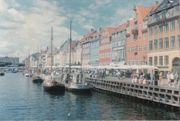 Nyhavn in Copenhagen: moored sailing boats, colorful townhouses, crowds along the quay