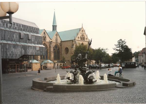 Bronze fountain in a paved square, Gothic church with spire behind