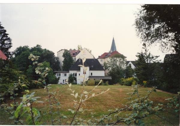 White houses with red roofs and church spire behind a grassy park