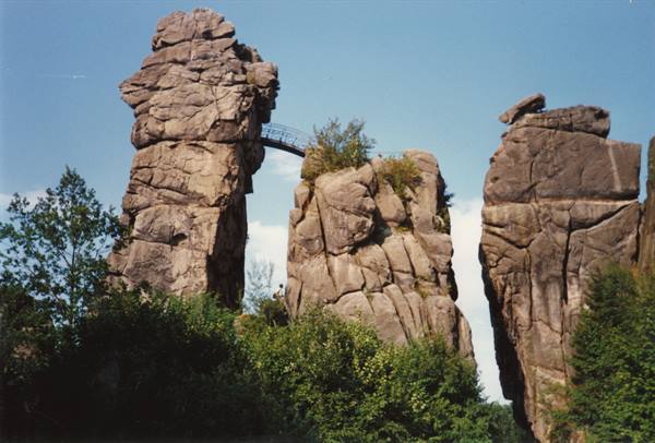 Towering sandstone rock pinnacles linked by iron bridge, Externsteine, green trees below