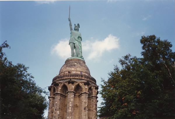Hermann statue raising sword atop the stone monument, trees under blue sky