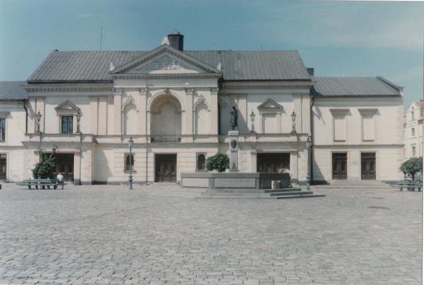 Neoclassical theater with pediment and statues, cobblestone square, daylight