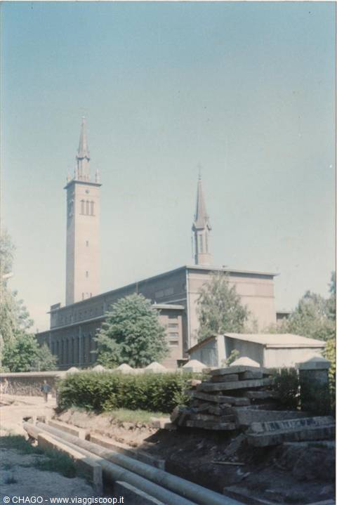 Brick church with tall bell tower and spire, pipes and construction site in front