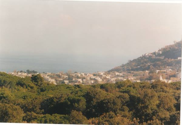 White houses at the foot of a green hill, hazy sea behind, diffused light