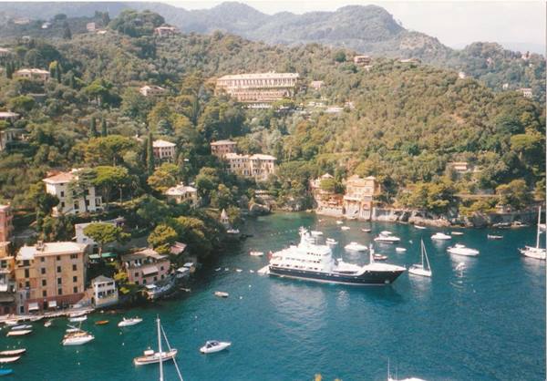 White yacht anchored in Portofino bay among colorful houses and green hills