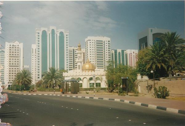 White mosque with golden dome among skyscrapers and palm trees in Abu Dhabi