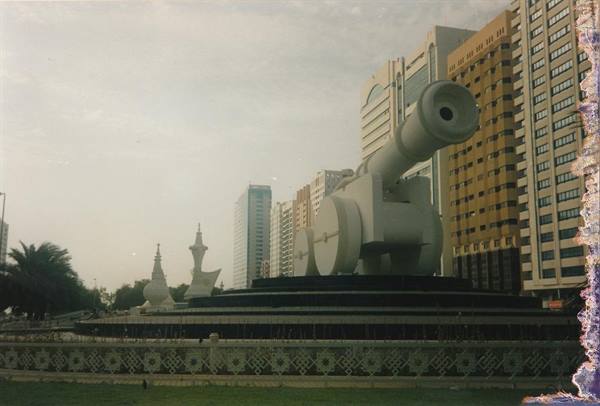 Roundabout with giant white cannon among skyscrapers and minarets, soft daylight