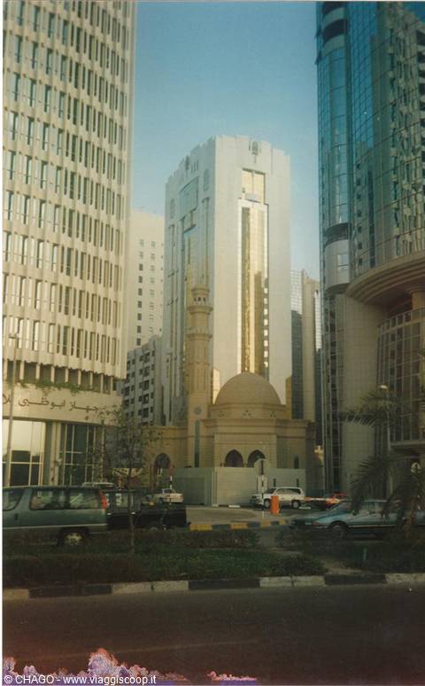 Small mosque with minaret and dome surrounded by skyscrapers in Abu Dhabi