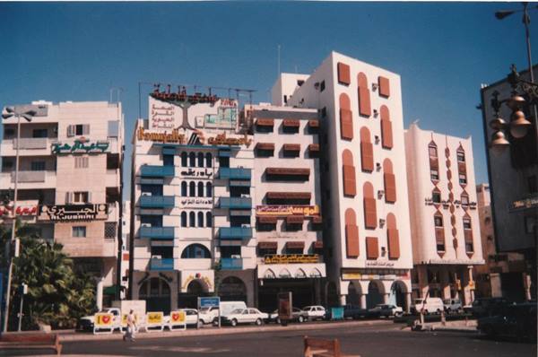 Buildings with Arabic signs and blue balconies under sunny sky, cars on street