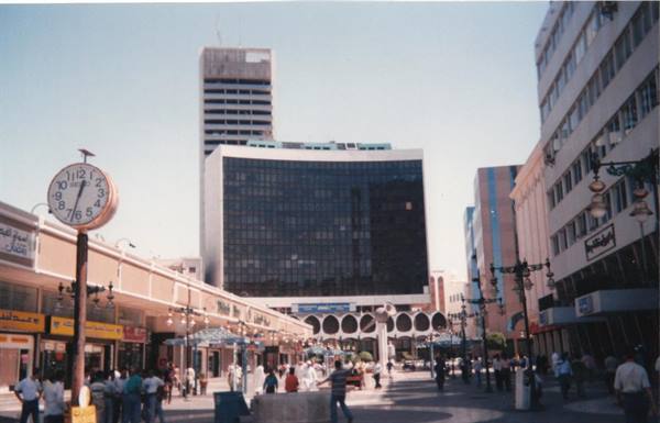 Clock on pole in pedestrian street, skyscrapers and pedestrians in a commercial district