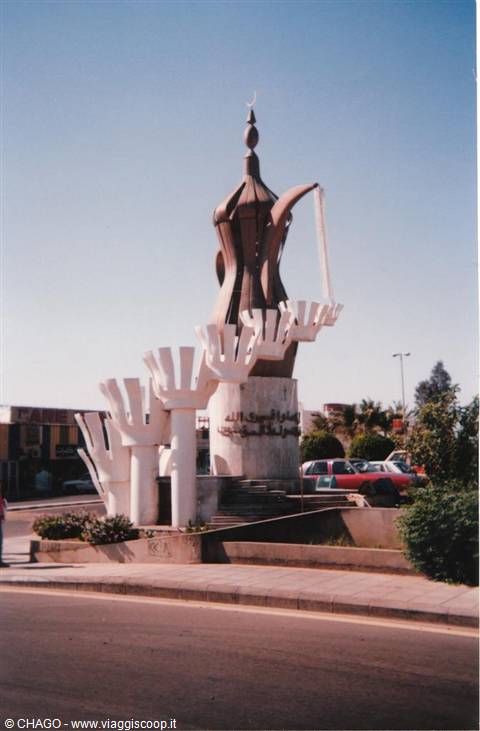 Giant coffeepot monument pouring cups at a sunny city roundabout