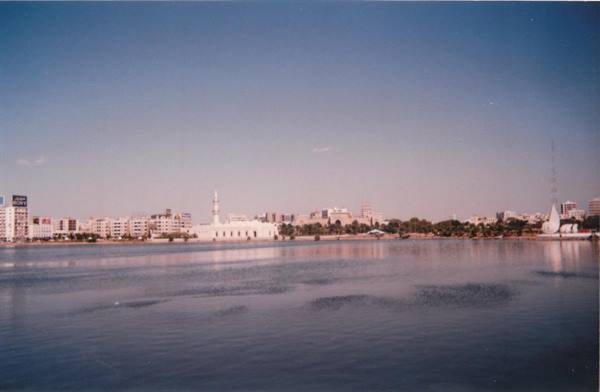 White mosque and minaret across the bay, low buildings under blue sky
