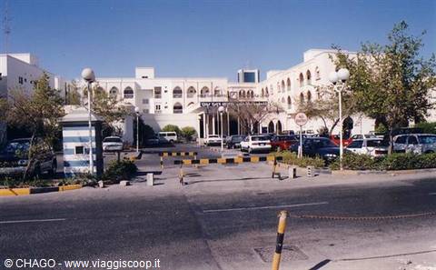 Hotel entrance with white arched facade, parking lot and guard post under sun