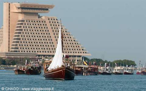 Wooden dhow with white sail in front of Doha's pyramid-shaped Sheraton hotel
