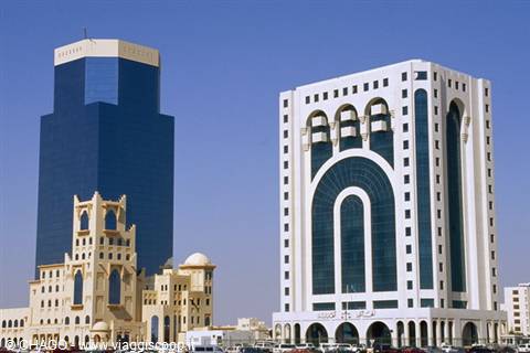 Modern skyscrapers in Doha: blue glass tower and white building with arches