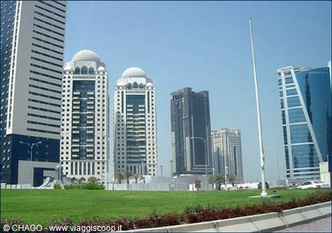 Domed skyscrapers in Doha, green lawn in foreground, clear blue sky