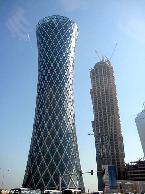 Curved glass skyscraper with diamond-pattern facade beside a building under construction